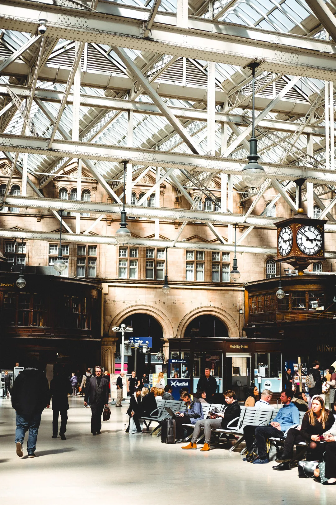 Interior of Glasgow Central Station, featuring individuals sat in waiting area awaiting trains, a ScotRail stand and station clock showing time of 2:50