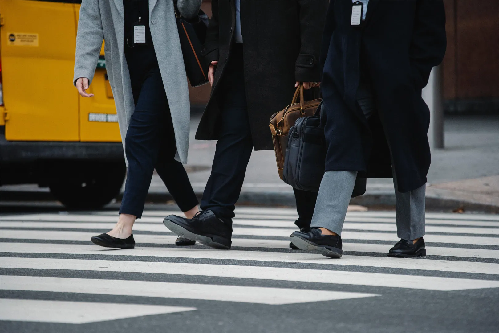 Three individuals wearing corporate outfits crossing a road using a zebra crossing, shot is focused primarily on their lower bodies with all heads and shoulders being excluded from the shot.