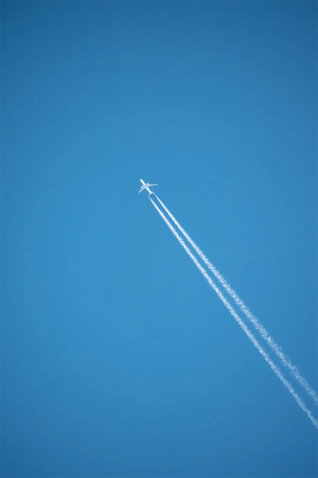 Shot of an airplane in a bright blue sky with two lines of vapour trails left behind the aircraft
