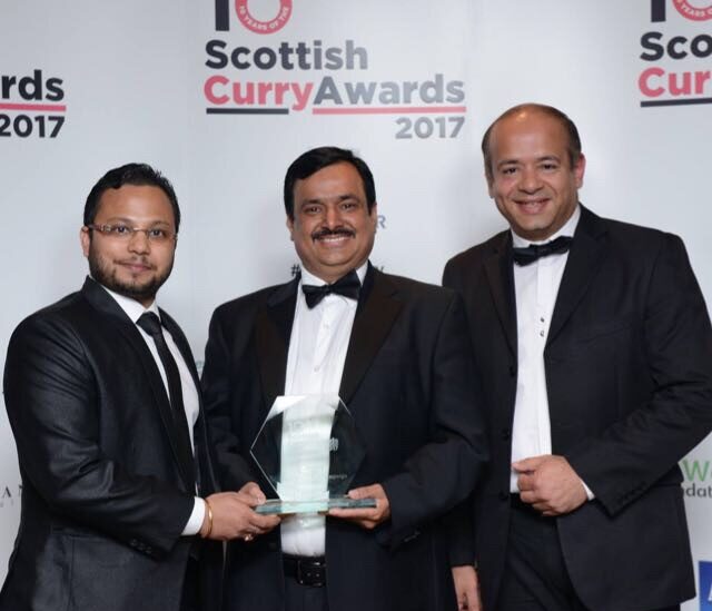 Three smiling men wearing black and white tuxedos accepting a glass award at the Scottish Curry Awards 2017