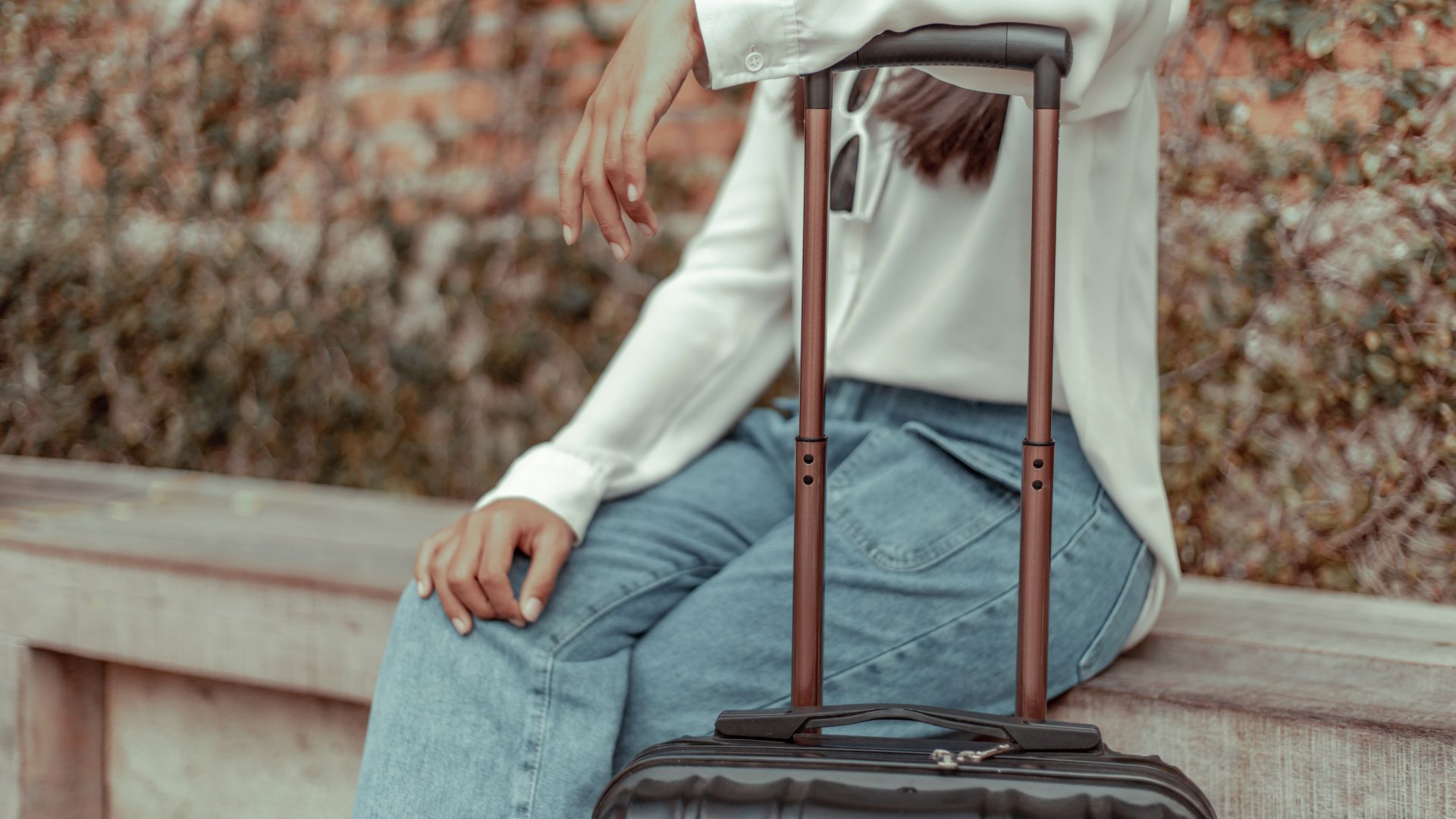 Seated female wearing a white shirt and blue jeans leaning on a suitcase handle